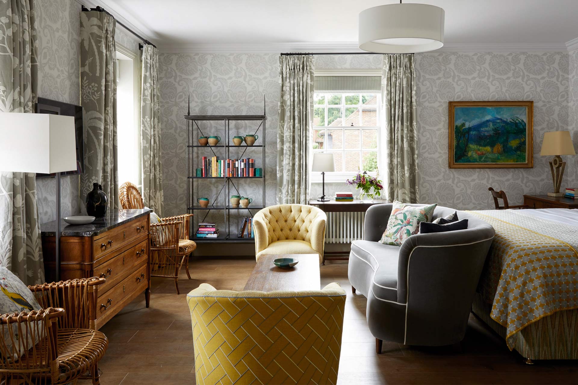 Suite sitting area with vintage bookshelf, painted armchair and floral bedspread at Brown's Hotel, Mayfair
